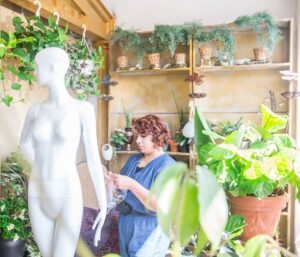A mannequin in a shop with plants in the background.