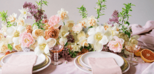A table setting with flowers and plates on a pink tablecloth.