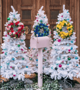 Three white christmas trees in front of a mailbox.