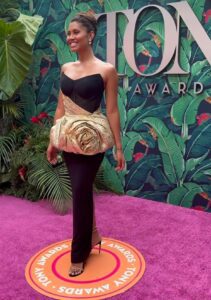 A woman is standing on a pink carpet at the tony awards.