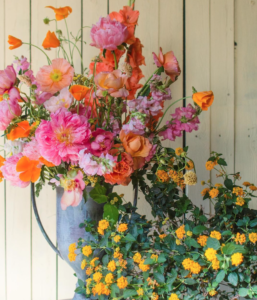 A vase filled with orange and yellow flowers on a wooden fence.