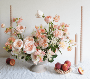 An arrangement of peaches and peonies on a table.